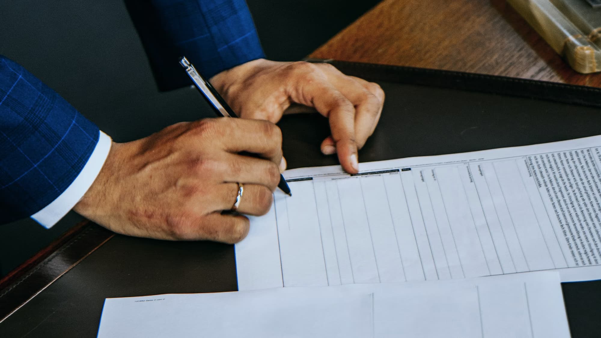 Main signant un document officiel posé sur un sous-main de cuir