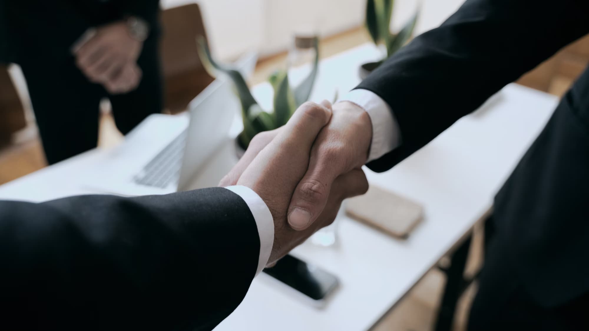 Poignée de main au-dessus d’une table de réunion, en tenue officielle