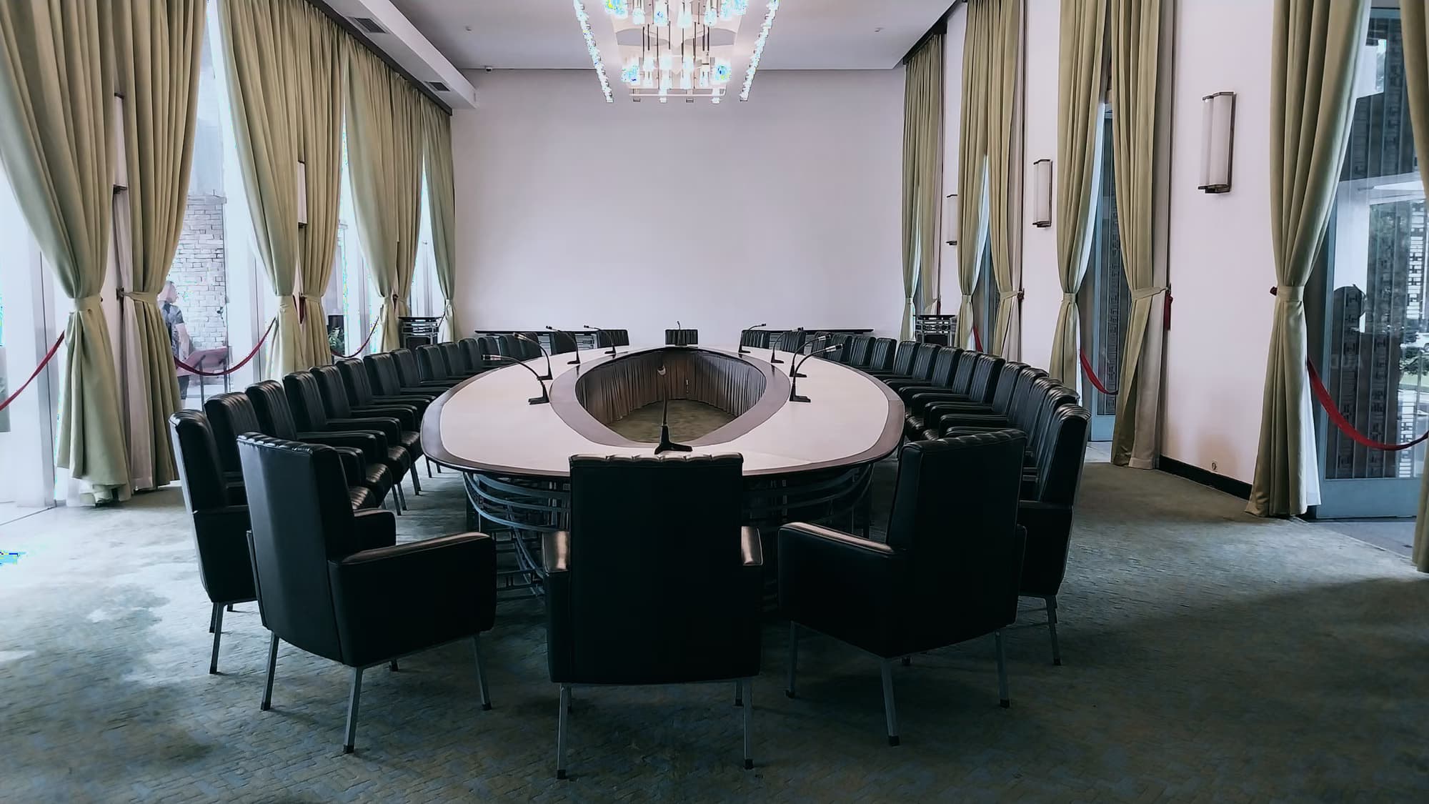 Salle de réunion en hémicycle, fauteuils et micros autour d’une table ovale