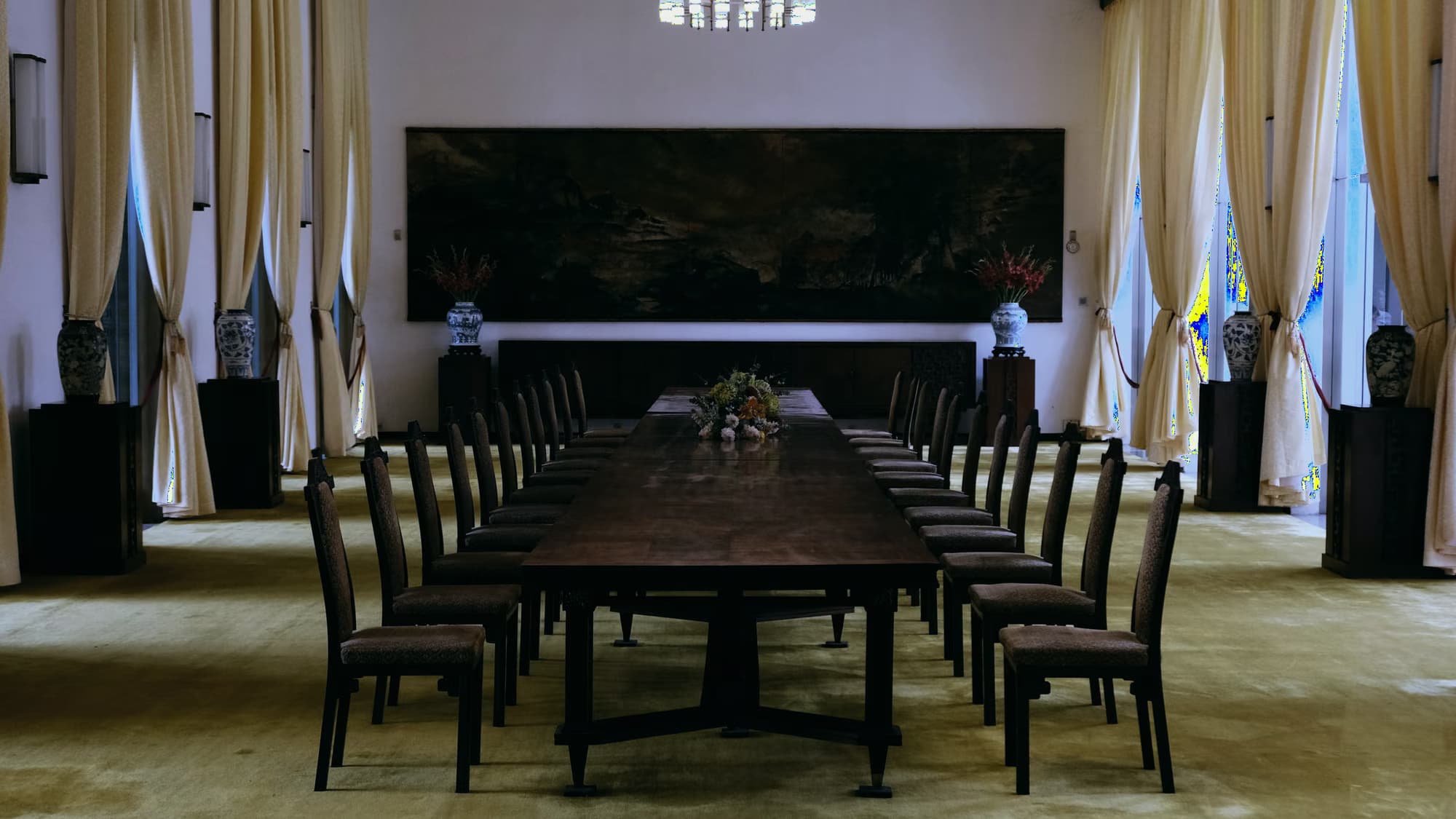 Salle d’honneur aux rideaux clairs, longue table de bois et chaises alignées