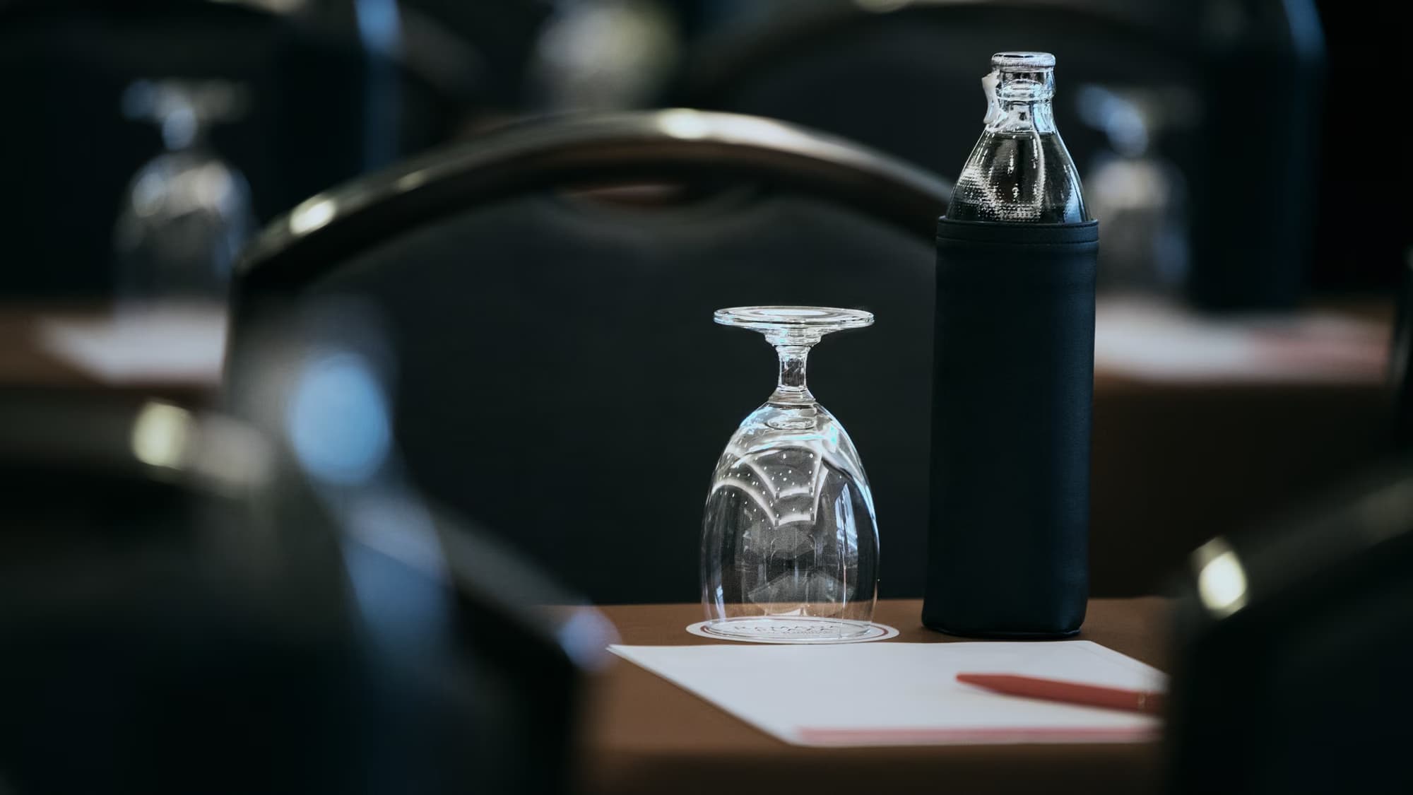 Table de séminaire dressée : verre retourné, bouteille d’eau et bloc de papier